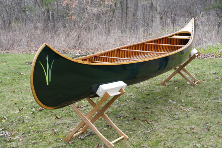 A dark green wooden canoe rests on supports in a grassy area.