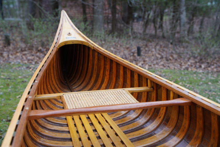 The interior of a wooden canoe showing the ash ribs and floorboards and caned bow seat.