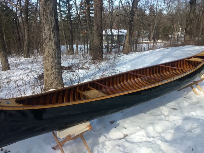 a dark green canoe with wooden frame sits on supports in a snowy woods
