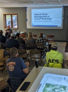 Workshop attendees are sitting and listenign to a presentation with the title slide "Natural Flood Management & Culvert Workshop" visible.