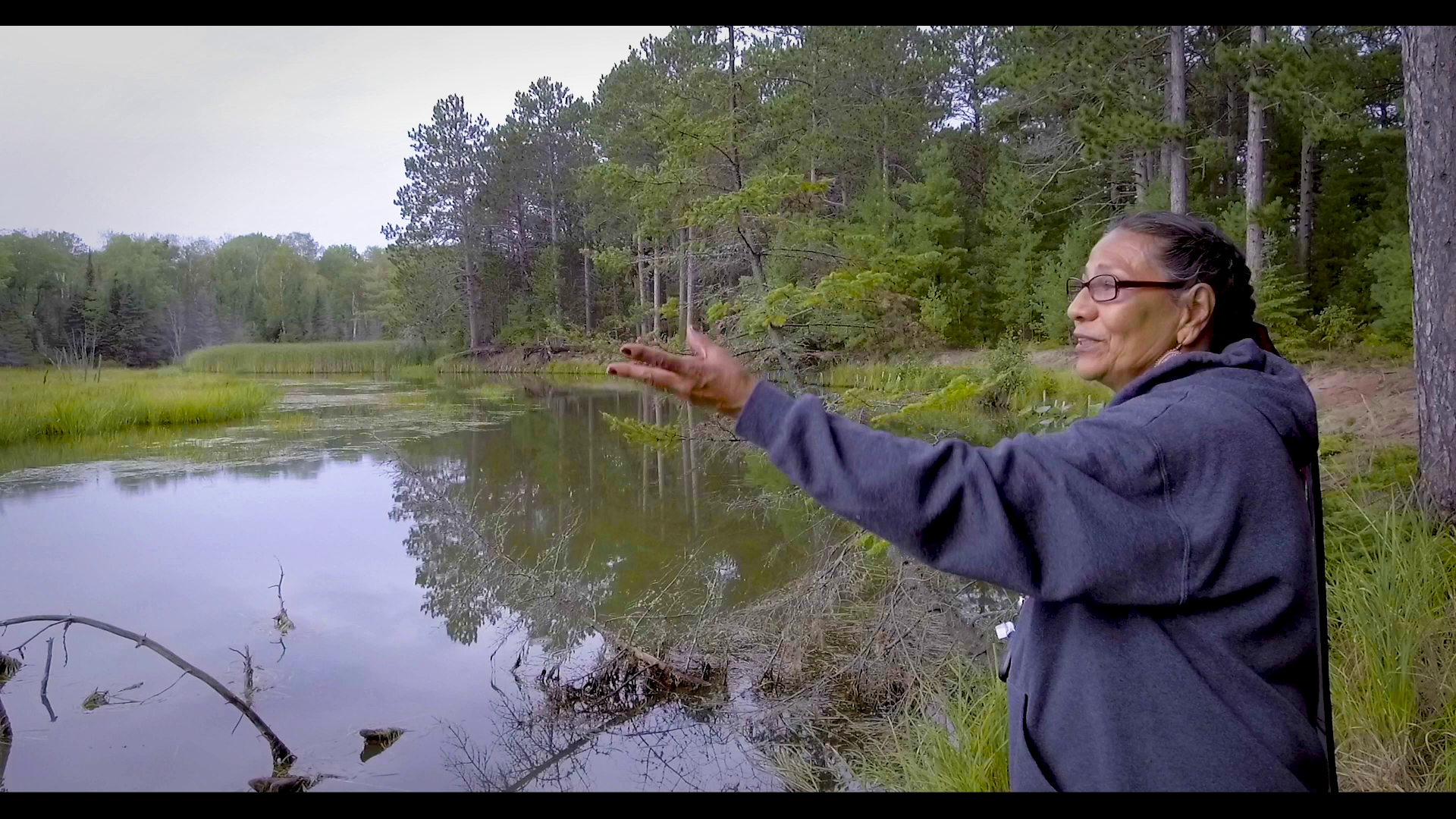 Carolyn L.C. Gouge-Powless, a member of the Red Cliff Band of Lake Superior Ojibwe Kwe, holds out a hand towards a wetland in the Red Cliff Reservation.