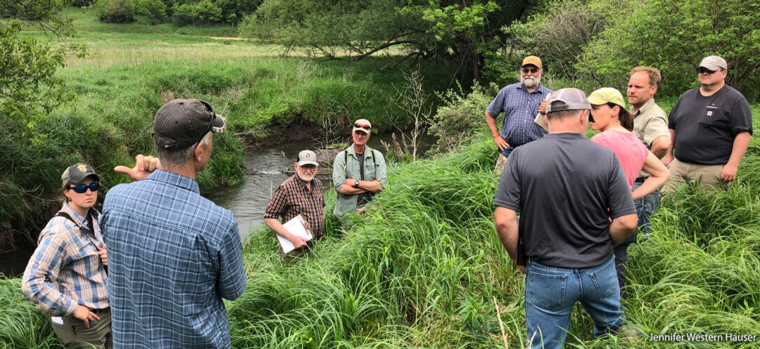 A photo of a group of people (including some WWA staffers) standing along a severely incised creek bed discussing how to restore the floodplain.