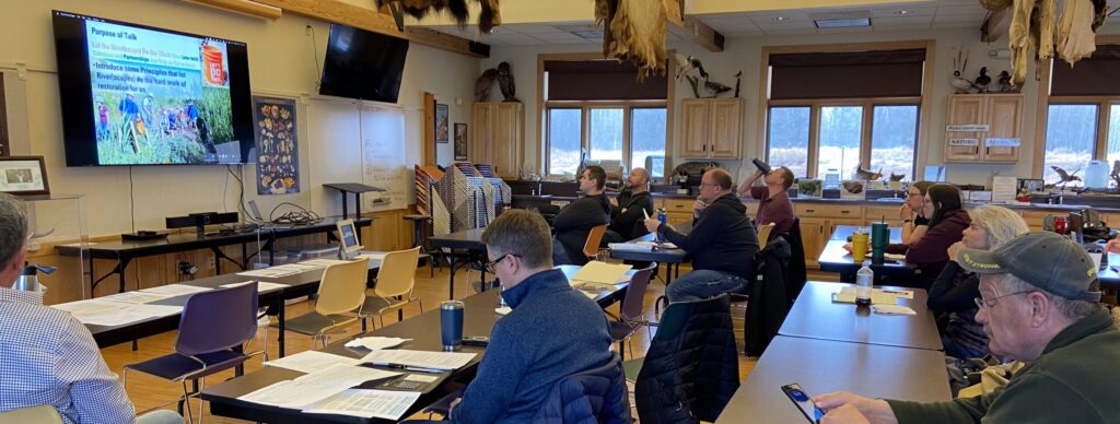 DATCP staff sit at tables inside a large conference room watching a presentation given by WWA staff.